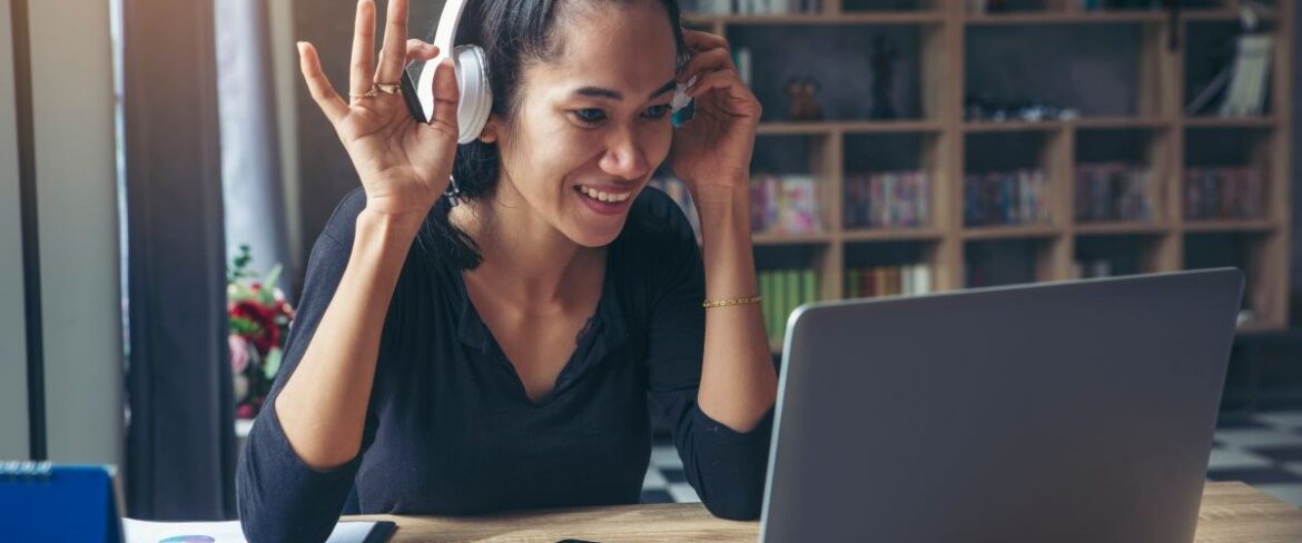 woman with headphones in front of laptop saying hi to someone on screen