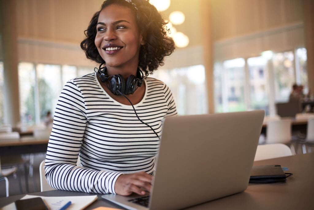 young female sitting at a table with a laptop and headphones