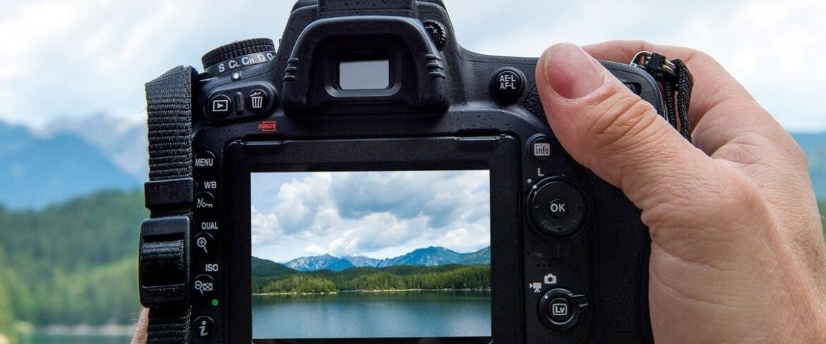 Person holding a camera taking a picture of a mountain and lake