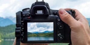 Person holding a camera taking a picture of a mountain and lake