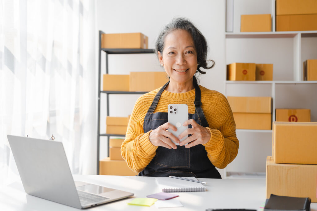 Asian woman standing in front of boxes with cell phone in hand