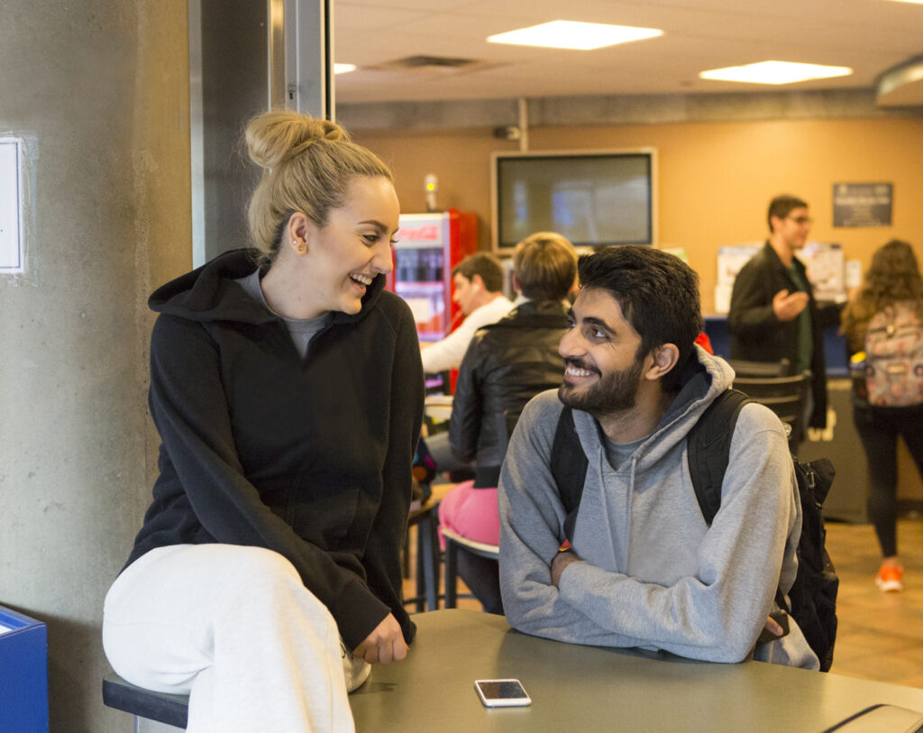 Two students looking at each other and smiling in the Student Union building cafe.