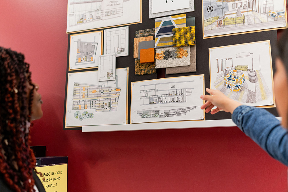 Students look at a set of interior design sketches. One student points to a drawing.