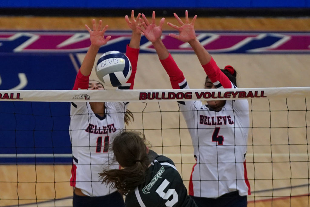 Two Bellevue volleyball players go up for a block