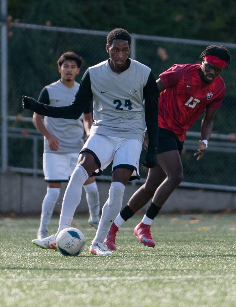 Sophomore Harryson Powell from the Men's Soccer team getting ready to kick the ball with other players crowding in.