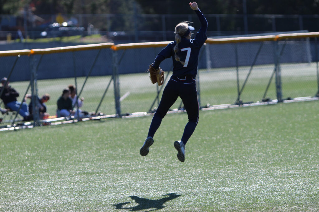 Softball player leaping into the air, one arm raised high.