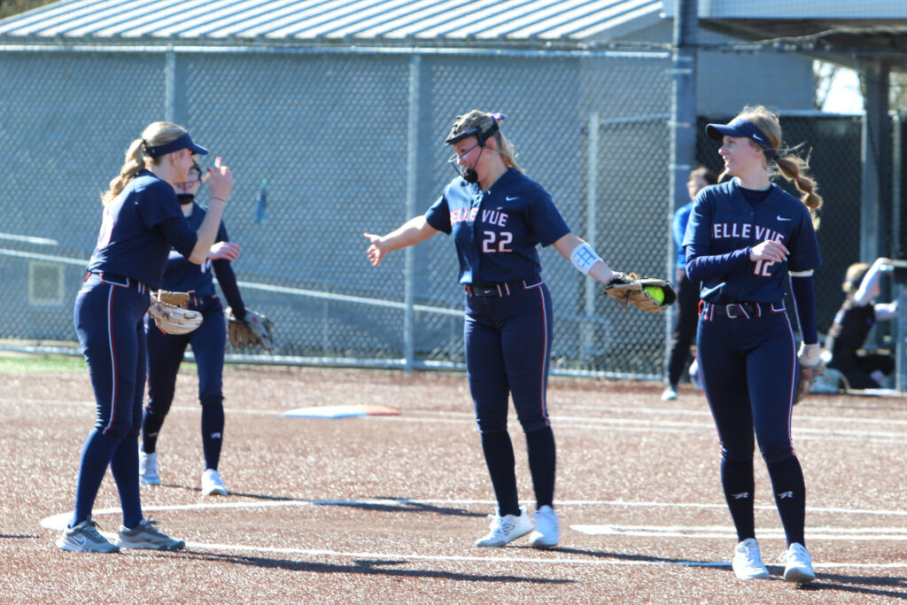 2026 Softball team members discussing a play during the game.