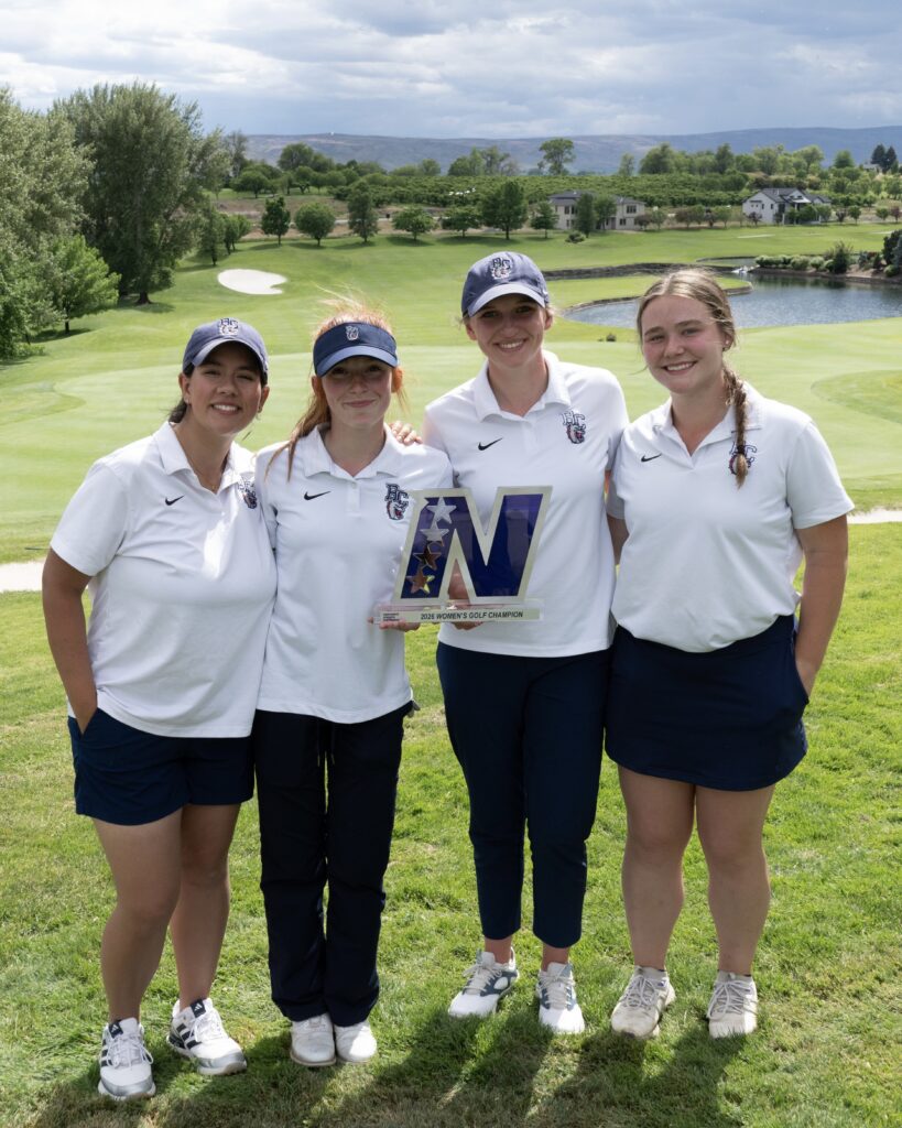 Women's golf team members in front of a lush green under overcast skies and clouds in the distance.