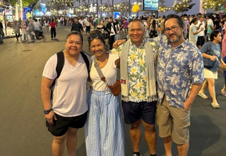 A group photo of 4 Cambodian adults standing in front of a busy night market in Cambodia