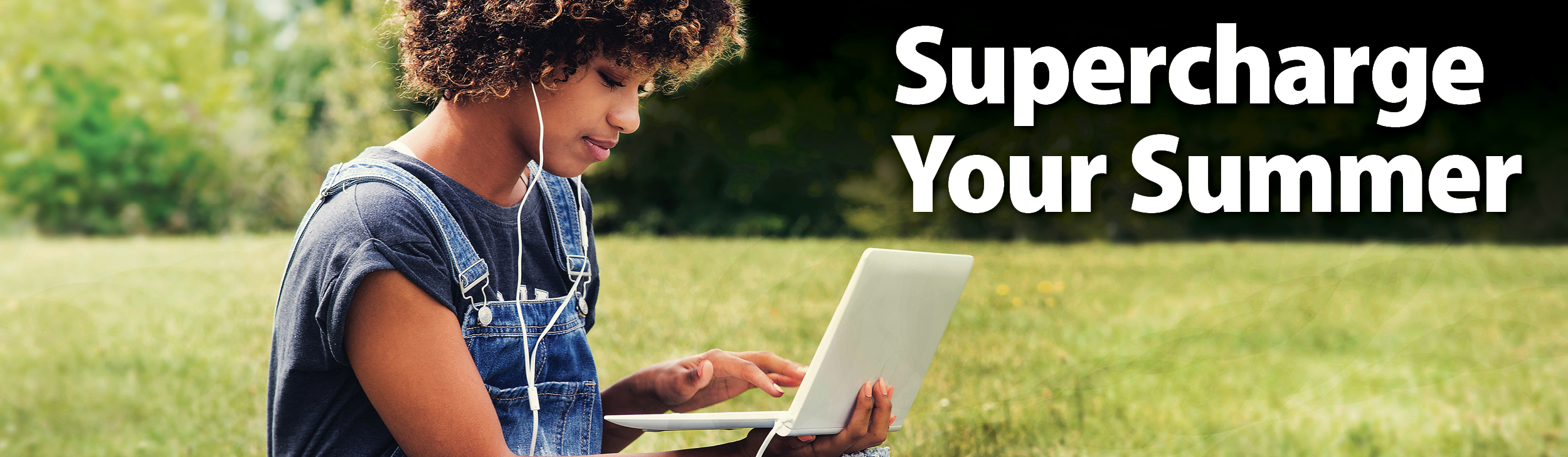 Supercharge Your Summer. Black female student working on laptop outside on the grass on a sunny day.