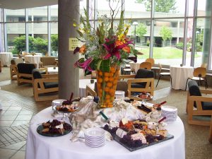 Catering spread with center piece and food around a table covered in white linen