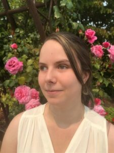 Headshot of Ali Steenis wearing a white shirt in front of pink roses.