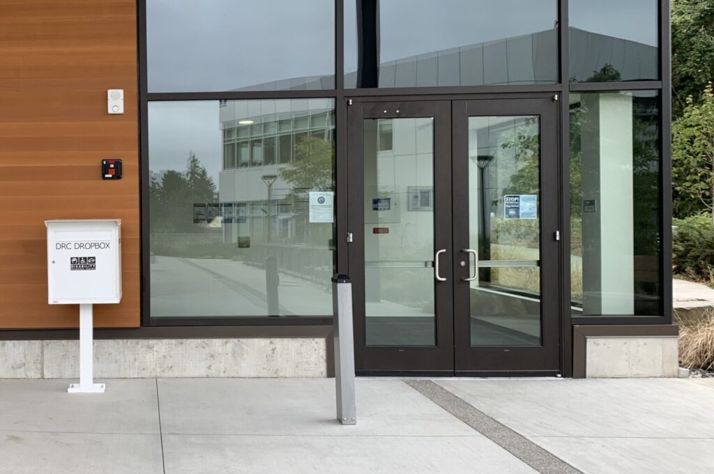 The ground floor entrance to the U Building. The entrance has double doors that pull to open. The DRC dropbox is to the left of the door.