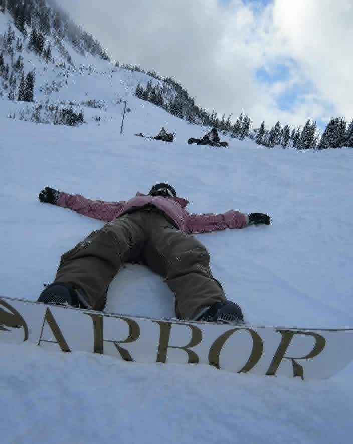Alma in snow gear on a snowboard laying on the ground with her arms out at Steven's Pass.
