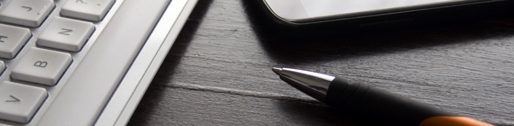 laptop, cellphone and orange pen on a wooden desk