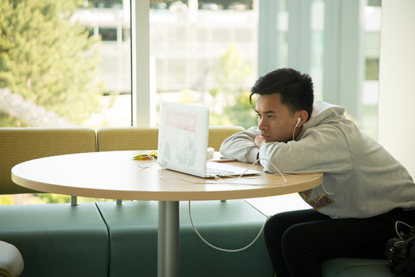A Bellevue College student wears earbuds while watching a video on a laptop.