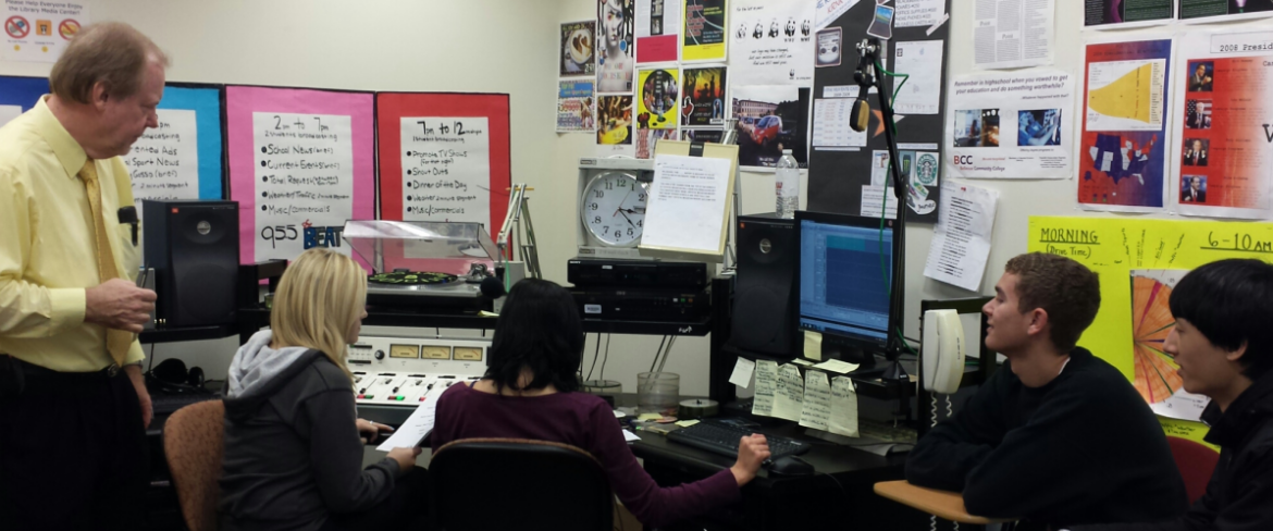 students in class working at a computer with their professor in the broadcasting class