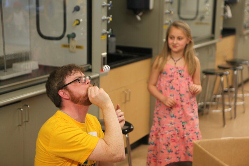 Physics Instructor Caleb Teel shows girl Bernoulli's principle with a straw and ping pong ball.