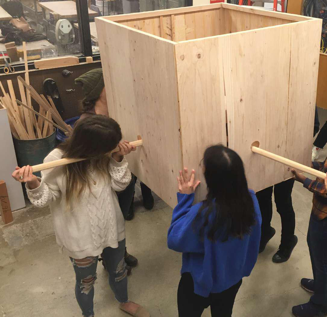 Students holding up a large wood box with dowels