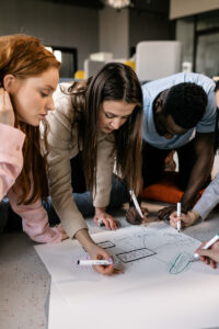Students map out a chart together, on the floor with large paper and markers.