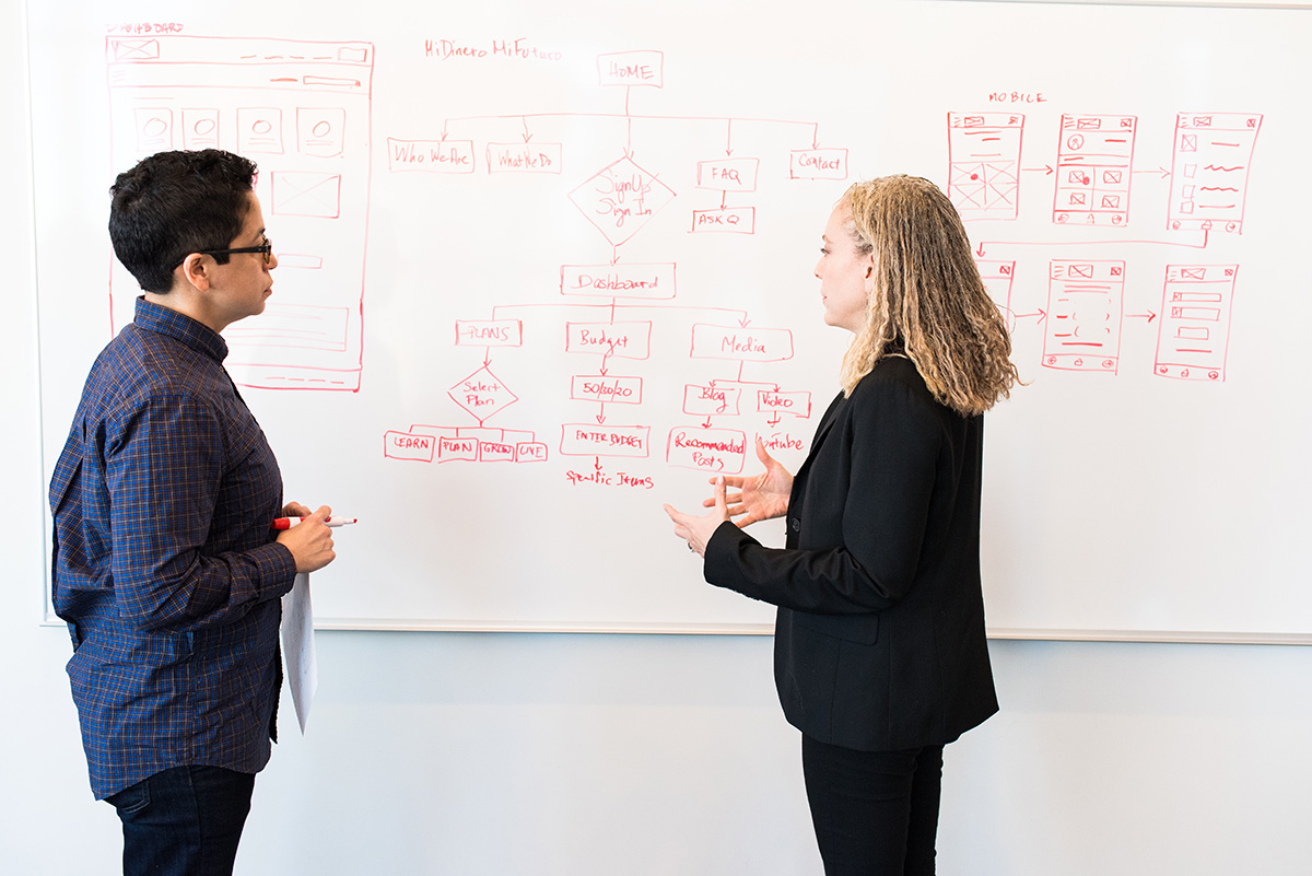 A student and teacher discuss in front of a whiteboard.
