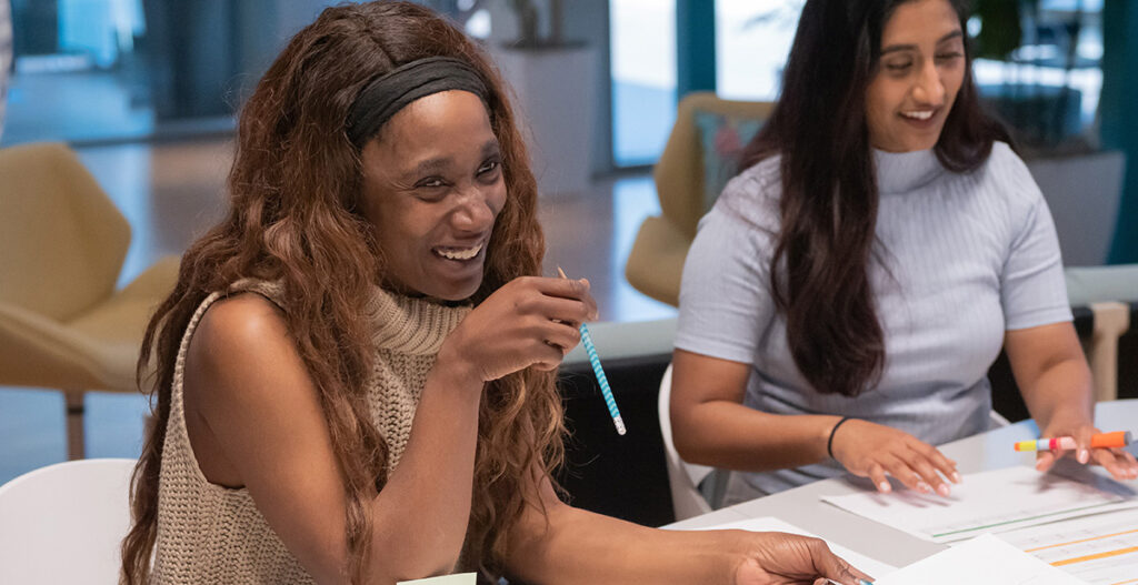 Two students smile while working on charts and graphs at a large table.