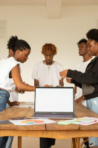 Students collaborate on a presentation at a large table, wtih a laptop and charts.