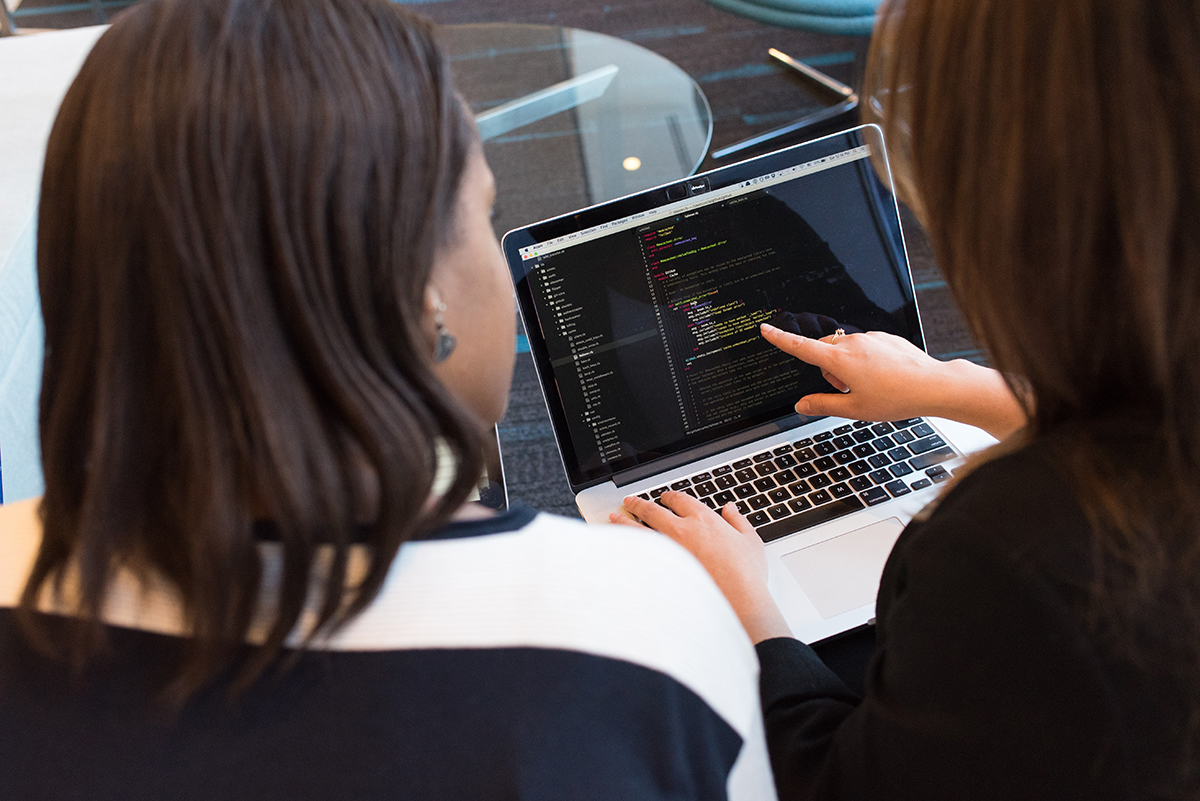 Two people collaborate over code on a laptop.