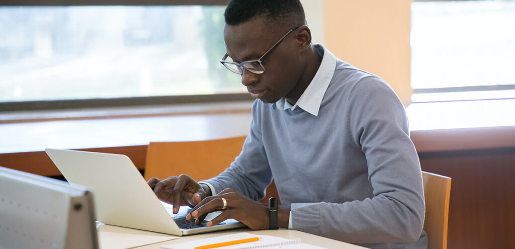A student works on a laptop by a window.