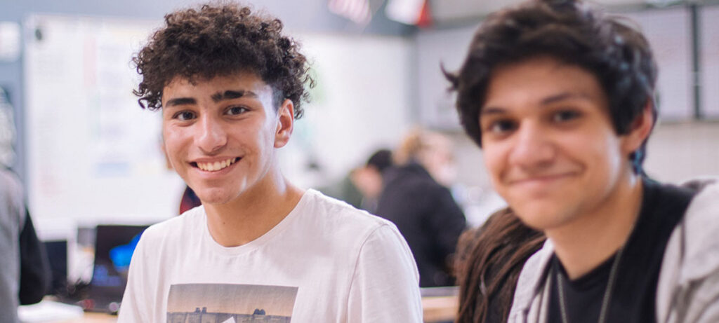 Two students smile while working together in a classroom.