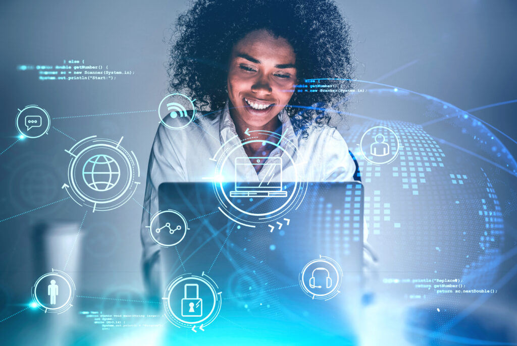 Cheerful young African American woman using laptop at blurry table with double exposure of creative online business interface. Concept of working from home during coronavirus pandemic. Toned image