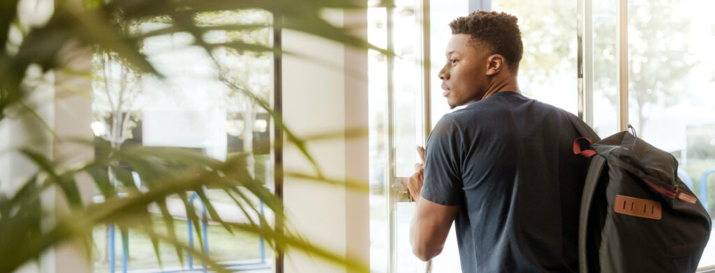 student with a backpack at a door is headed outside