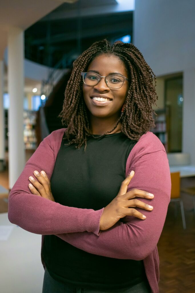 female-presenting student with locks and glasses, smiling and crossing their arms