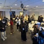 A group of students participates in a hands-on VR experience in a classroom setting. Many are wearing VR headsets and holding controllers, actively engaged in virtual activities. Others are observing, chatting, or preparing equipment. A poster on the back wall reads “XR LAB – BC Library Classroom,” indicating the event is hosted by Bellevue College’s XR Lab. The room is equipped with white chairs, projectors, and tables filled with gear, creating a lively and interactive learning environment.